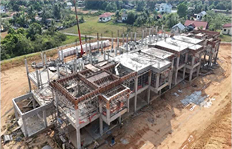 Aerial view of a reinforced concrete building frame rising from red laterite ground