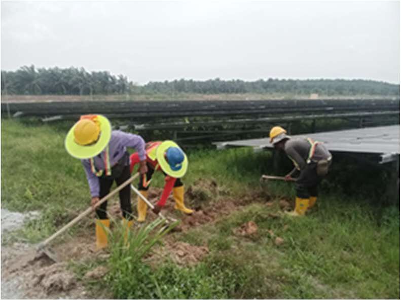 Workers in hard hats digging a drain between rows of solar panels